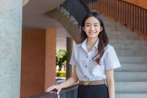hermosa joven estudiante asiática está sonriendo y mirando la cámara en el fondo de la universidad. foto
