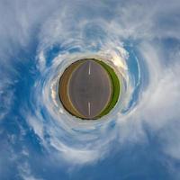 tiny planet in blue overcast sky with beautiful clouds with transformation of spherical panorama 360 degrees. Spherical abstract aerial view. Curvature of space. photo