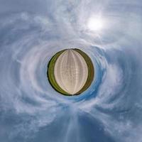 tiny planet in blue overcast sky with beautiful clouds with transformation of spherical panorama 360 degrees. Spherical abstract aerial view. Curvature of space. photo