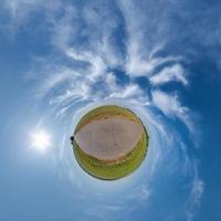 tiny planet in blue overcast sky with beautiful clouds with transformation of spherical panorama 360 degrees. Spherical abstract aerial view. Curvature of space. photo