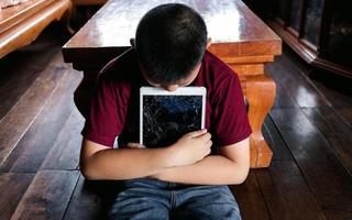 Portrait of a little Asian boy, Kid sad face, Unhappy child sitting hug broken tablet computer, Emotion sad and sad face, depressed children concept photo