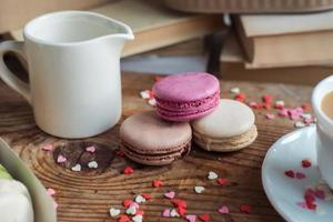 Macaroons and a cup of coffee, a milk jug on a background of small hearts on a wooden background, top view photo