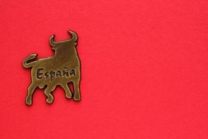 Metal souvenir fridge magnet of bull Spain isolated on red background. Travel memory concept. Gift typical product for tourists from trip. Home decor. Top view, flat lay, close up. Copy space for text photo