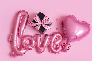 Foil balloon in love and heart shape with gift box on pink background. Valentines Day concept photo