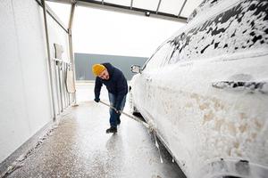 Man washing american SUV car with mop at a self service wash in cold weather.