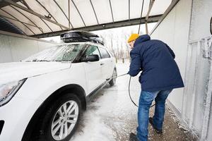 Man washing high pressure water american SUV car with roof rack at self service wash in cold weather. photo