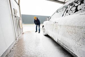 Man washing american SUV car with mop at a self service wash in cold weather.