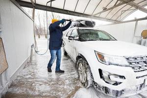 Man washing high pressure water american SUV car with roof rack at self service wash in cold weather. photo