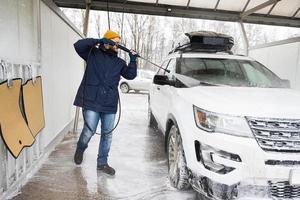 Man washing high pressure water american SUV car with roof rack at self service wash in cold weather. photo