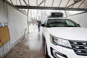 Man washing high pressure water american SUV car with roof rack at self service wash in cold weather. photo