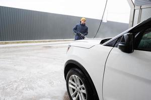 hombre lavando agua a alta presión coche suv americano en lavado de autoservicio en clima frío. foto