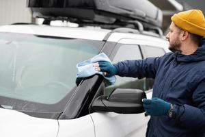 Man wipes american SUV car windshield with a microfiber cloth after washing in cold weather. photo