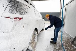 hombre lavando un camión suv americano con un trapeador en un lavado de autoservicio en clima frío. foto