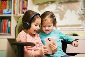 Two little girls sisters wear headphones watching cartoons or kid video on mobile phone. photo