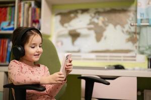 Little girl wear headphones watching cartoons or kid video on her phone. photo