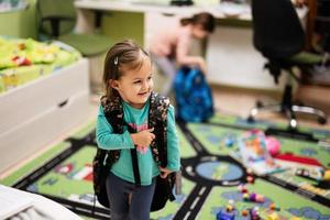 Young lovely baby girl with a big backpack in the interior of room. Getting ready for school. photo