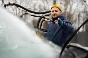 el hombre limpia el parabrisas de un vehículo suv americano con un paño de microfibra después de lavarlo en clima frío. foto