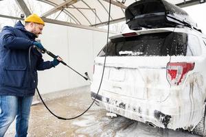 Man washing high pressure water american SUV car with roof rack at self service wash in cold weather. photo