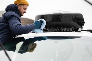 el hombre limpia el portaequipajes del camión suv americano con un paño de microfibra después de lavarlo en clima frío. foto