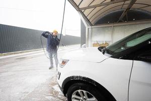 hombre lavando agua a alta presión coche suv americano en lavado de autoservicio en clima frío. foto