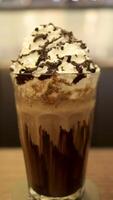 Chocolate milk shake full of cream and melted chocolate in a high glass at the table. photo