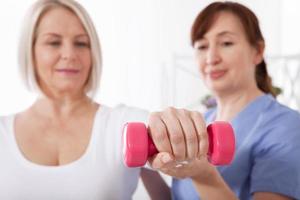 fisioterapia de rehabilitación moderna. fisioterapeuta ayuda a una mujer de mediana edad a recuperarse de una lesión mediante el ejercicio con pesas. foto