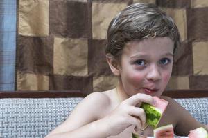 A cheerful boy eats watermelon at home at the table, home comfort, the warmth of the family hearth photo