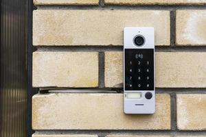 an intercom on the door of a private house, an intercom panel with a video camera on a brick beige fence post photo