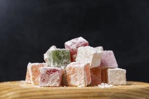 Sweet delicious colored lukum, Turkish delight with powdered sugar on a black background. photo