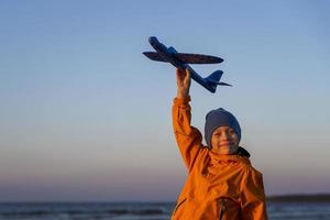 retrato de un chico lindo sosteniendo un avión en la mano contra un cielo azul, el camino hacia un sueño, el camino hacia el cielo foto
