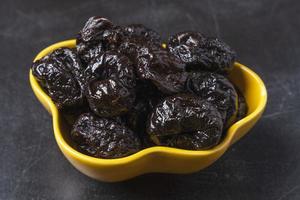 Sweet delicious prunes in a yellow plate on a black background. Delicious natural delicacy, dessert photo