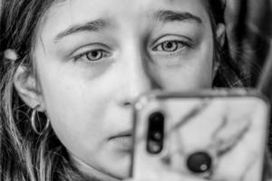 A teenage girl looks at a smartphone and cries. Sad girl with tears in her eyes. photo