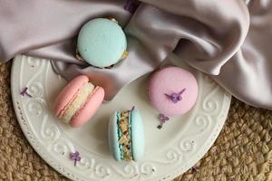 coloridos macarons de postre francés o macarons en un plato con flor lila sobre un fondo de tela de paja y atlas.