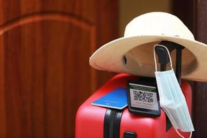 New normal concept. Close up view of a smartphone with an immune digital health passport, a red suitcase, protective mask, straw hat, passport and sunglasses. Traveling by plane during a pandemic. photo