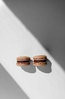 two sweet brown chocolate french macaroons or macarons dessert isolated on white background with light rays from window. copy space. photo