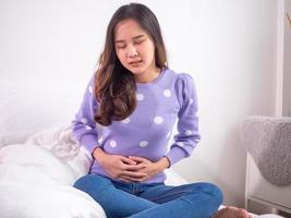 una mujer tiene malestar estomacal, tensa con una mano presionando el estómago. calambres menstruales foto