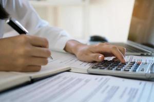 Asian businessmen work with calculators to calculate account information. In the office, work desks with documents and computers photo