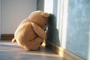 concepto infantil de tristeza. el oso de peluche sentado solo contra la pared de la casa, se ve triste y decepcionado. foto