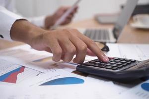 Pictures of businessmen are pressing the calculator to calculate business information. Documents and graphs about accounting are on the table. photo