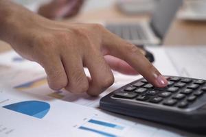 Pictures of businessmen are pressing the calculator to calculate business information. Documents and graphs about accounting are on the table. photo