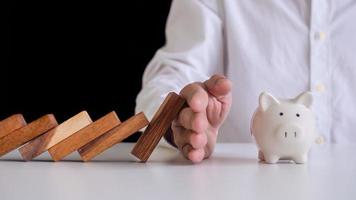 Insurance agents or family leaders are using hands to prevent domino from falling into the piggy bank . Prevention of external hazards. money insurance plan