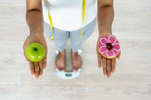 Women are choosing the right food for good health. Women are fasting. Comparison options between donuts and green apples during weight measurement on digital scales. photo