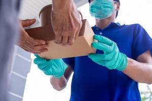 The shipper wears a mask and gloves, delivering food to the home of the online buyer. stay at home reduce the spread of the covid-19 virus. The sender has a service to deliver products or food quickly photo