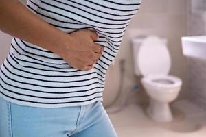Women are standing in front of the bathroom door using their hands to hold the abdomen with severe abdominal pain or diarrhea. The concept of stomach cramps, diarrhea photo