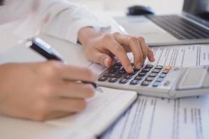 Asian businessmen work with calculators to calculate account information. In the office, work desks with documents and computers photo