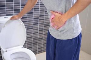 los hombres tienen dolor de estómago y usan sus manos para sostener su estómago en el baño. estreñimiento o cáncer de colon foto