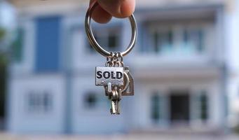 sold house key and blurry home on background photo