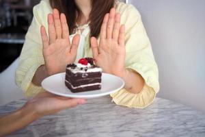 una mujer en el cuidado de la salud usa una mano para empujar un pastel de chocolate. se negó a comer alimentos que contienen grasas trans foto