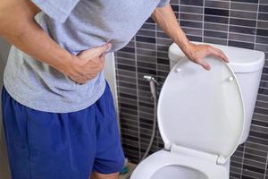 los hombres tienen dolor de estómago y usan sus manos para sostener su estómago en el baño. estreñimiento o cáncer de colon foto