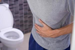 los hombres tienen dolor de estómago y usan sus manos para sostener su estómago en el baño. estreñimiento o cáncer de colon foto